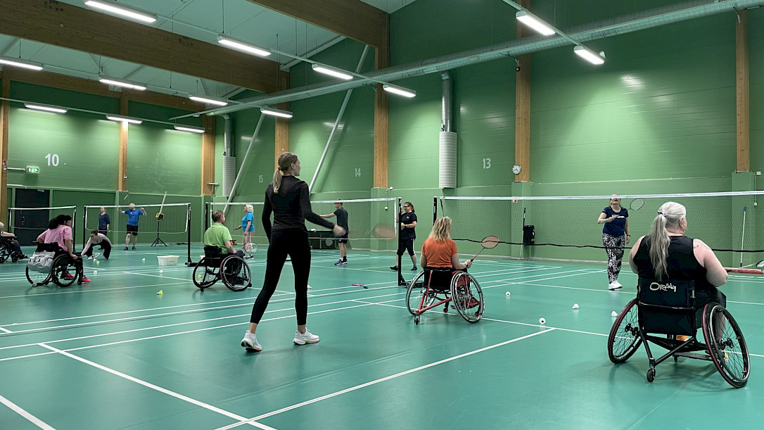 People of different functional abilities playing badminton on 4 full courses. Both standing players and people using wheelchairs.